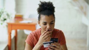 Woman looking at phone with credit card in hand examining spending